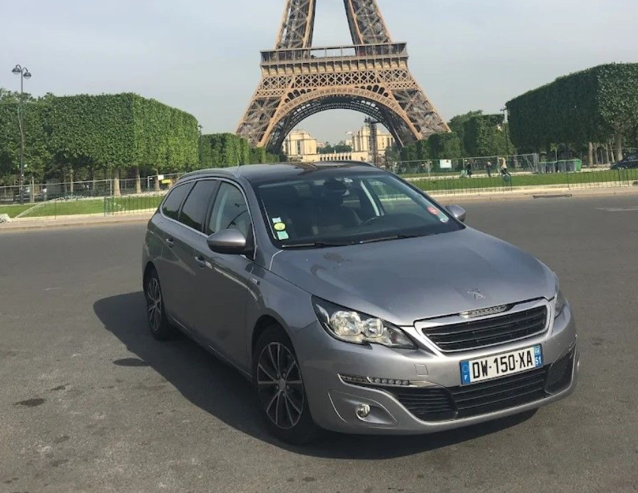 Un taxi noir est garé sur l'herbe devant des arbres.