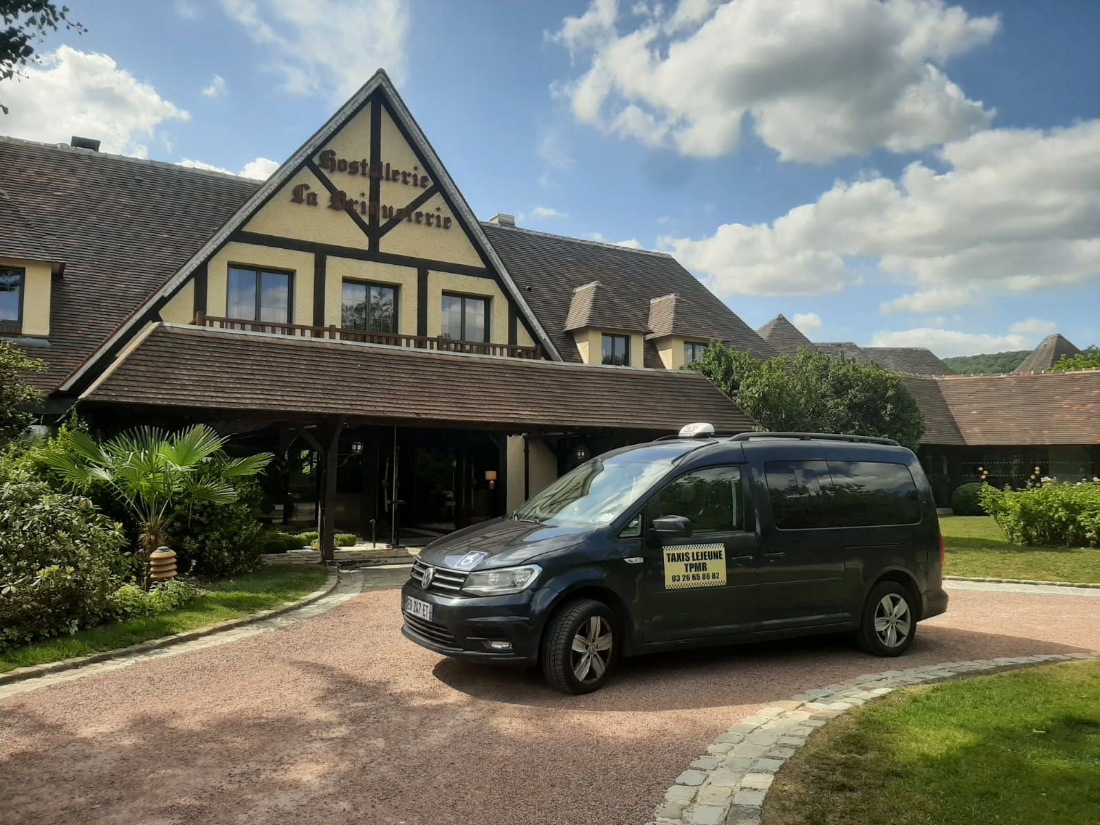 Un taxi van noir est garé devant un hôtel au toit marron par une journée ensoleillée.