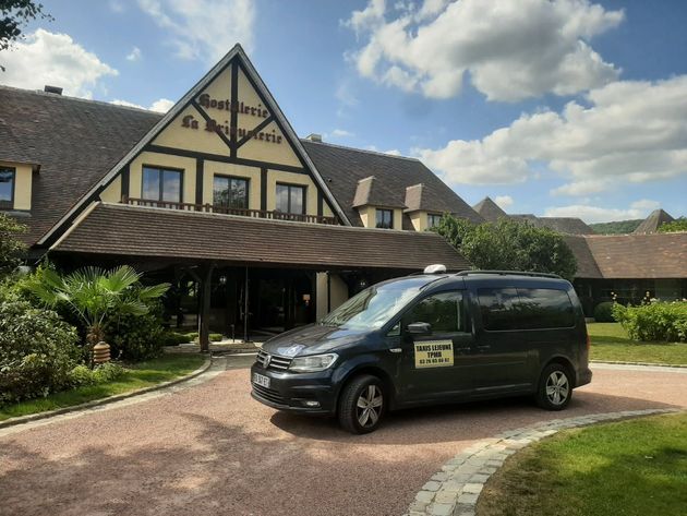 Un taxi van noir est garé devant un hôtel au toit marron par une journée ensoleillée.