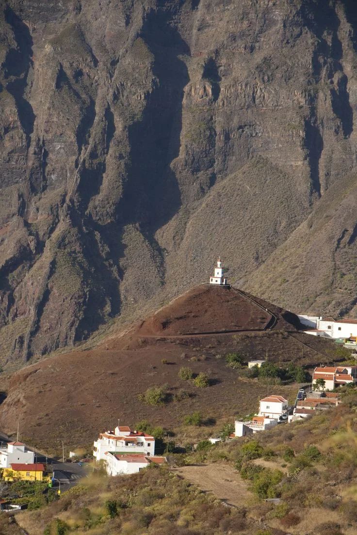 Un pequeño pueblo está situado en la cima de una colina rodeado de montañas.