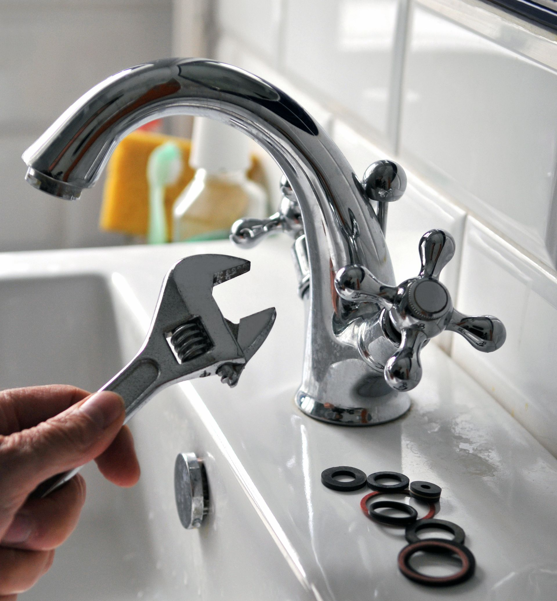 Main tenant une clé à molette, fixant un robinet chromé dans un évier, avec des rondelles de rechange.