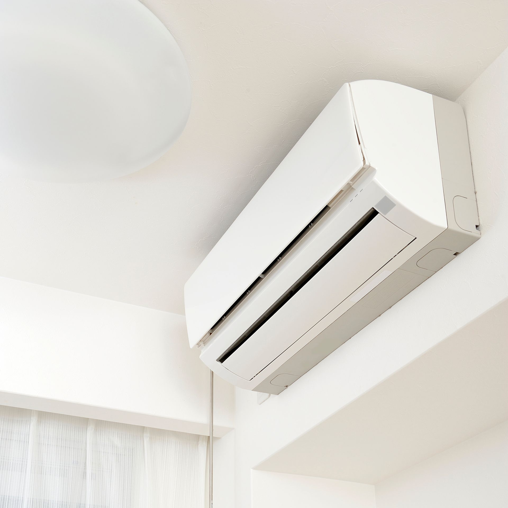 Climatiseur mural dans un coin d'une pièce avec un plafonnier et une fenêtre.