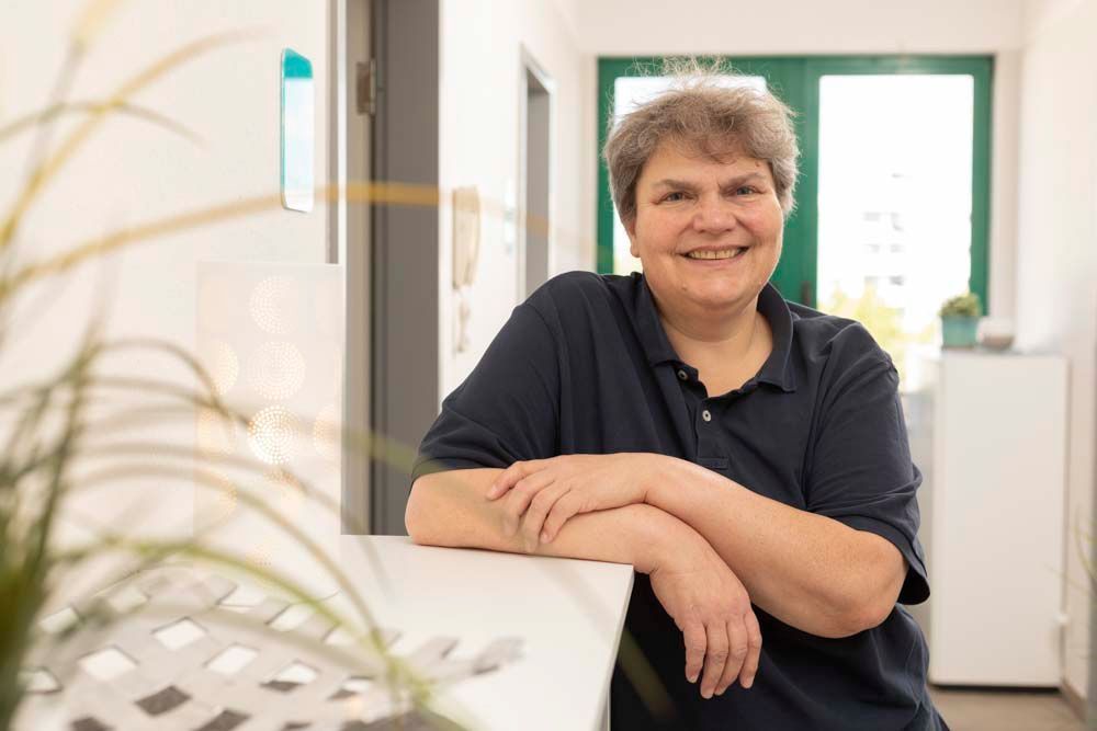 Eine Frau mit einem schwarzen T-Shirt mit der Aufschrift „Logopädie Praxis A. Busch“ lächelt in die Kamera.