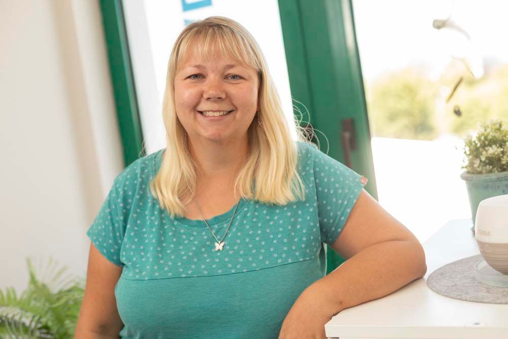 Eine Frau mit langen blonden Haaren trägt ein schwarzes Hemd und lächelt.