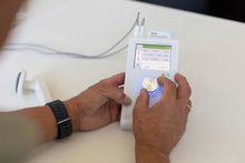 Eine Person verwendet ein weißes medizinisches Gerät mit Bildschirm und Drehknopf, das mit Kabeln verbunden ist. Sie nimmt Einstellungen am Gerät vor.