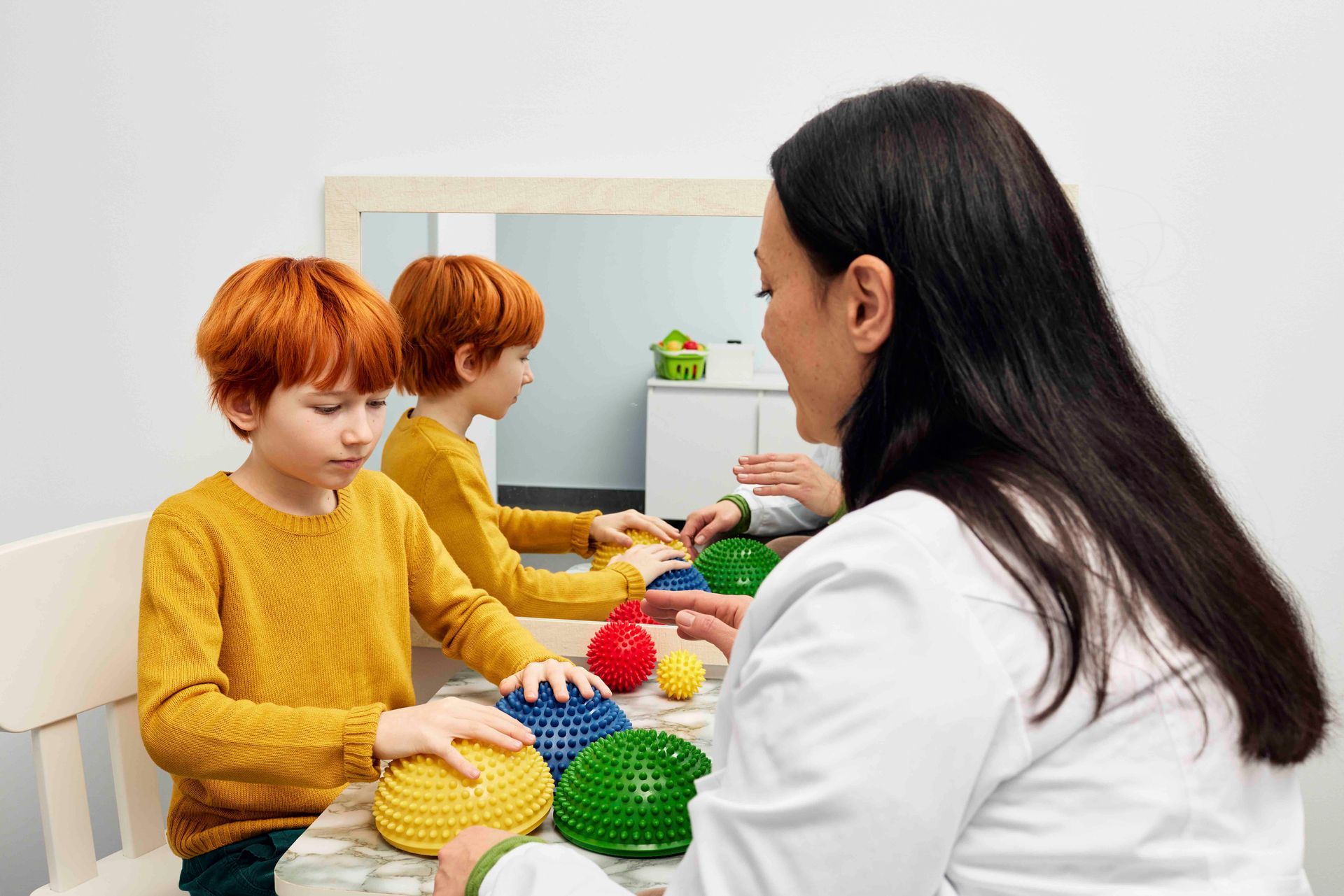 Eine Frau sitzt mit zwei Kindern an einem Tisch, die mit Spielzeug spielen.