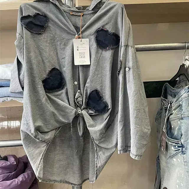 Una camisa gris con parches está colgada en un perchero.