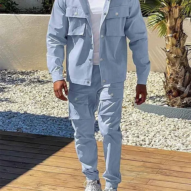 Un hombre que viste una chaqueta y pantalones de color azul claro está de pie sobre una plataforma de madera.