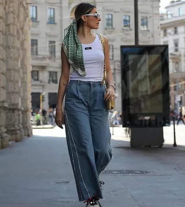 Una mujer que viste una camiseta blanca sin mangas y jeans anchos camina por la calle.
