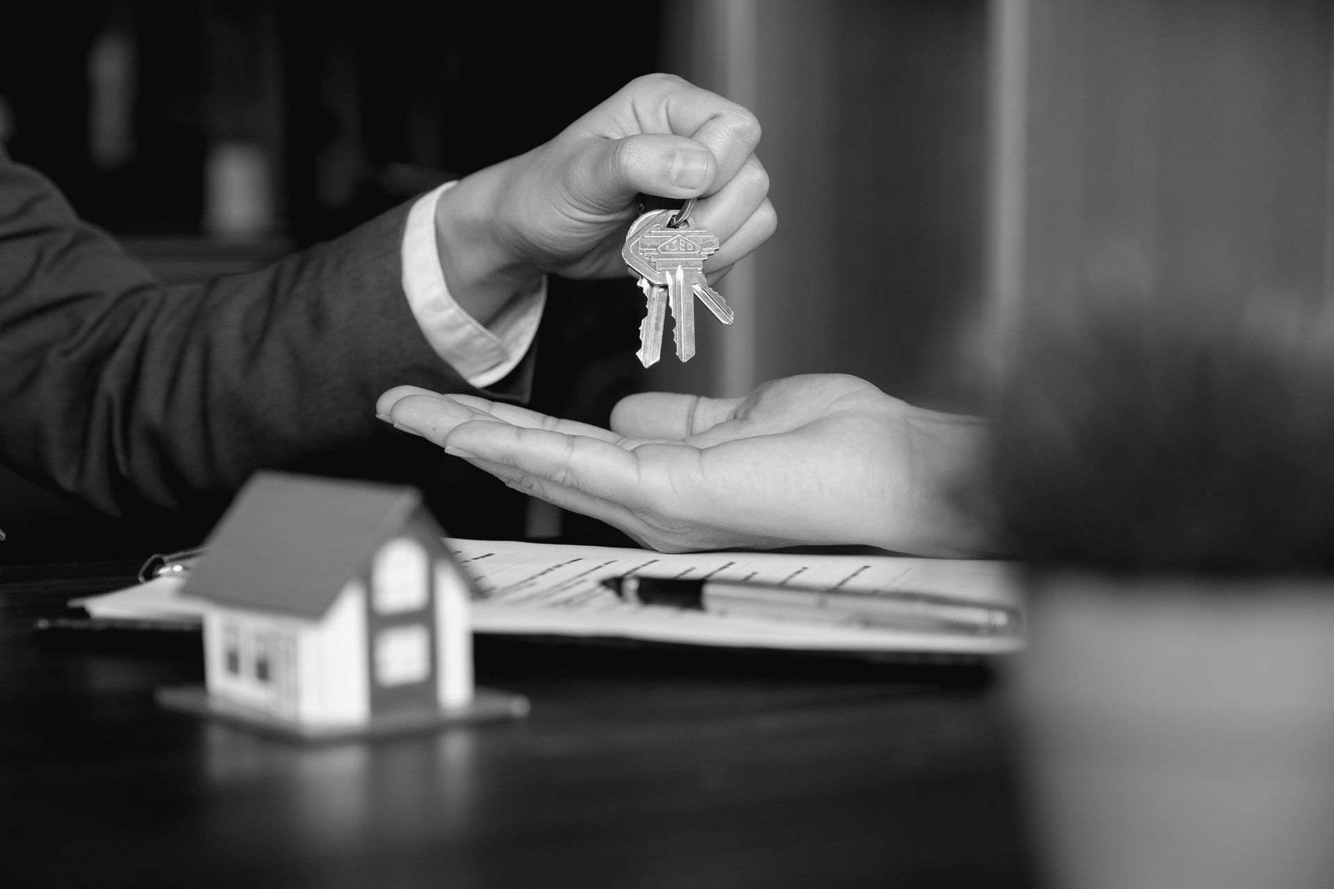 Un homme de loi posant des clefs dans la main d'un acquéreur par-dessus un bureau où trône une maquette de maison 