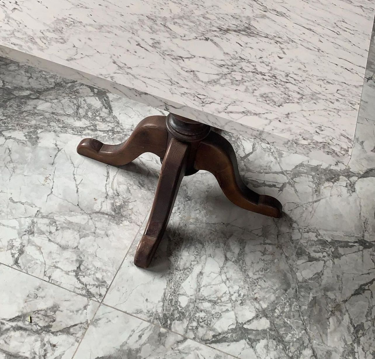 Una mesa con base de madera está colocada sobre un suelo de mármol.