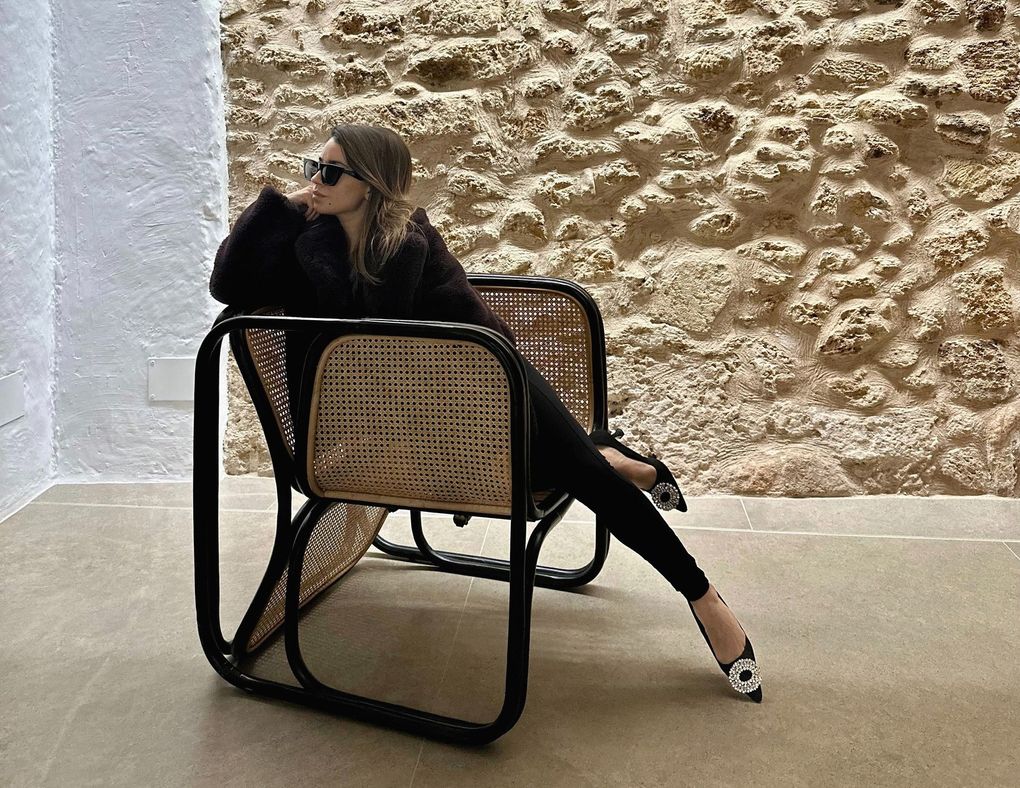 Una mujer está sentada en una silla frente a un muro de piedra.