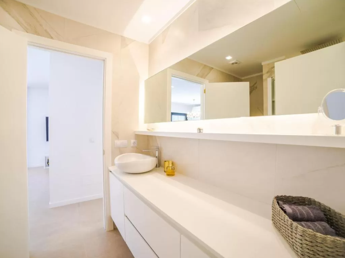 Un baño con lavabo, espejo y cesta de mimbre.