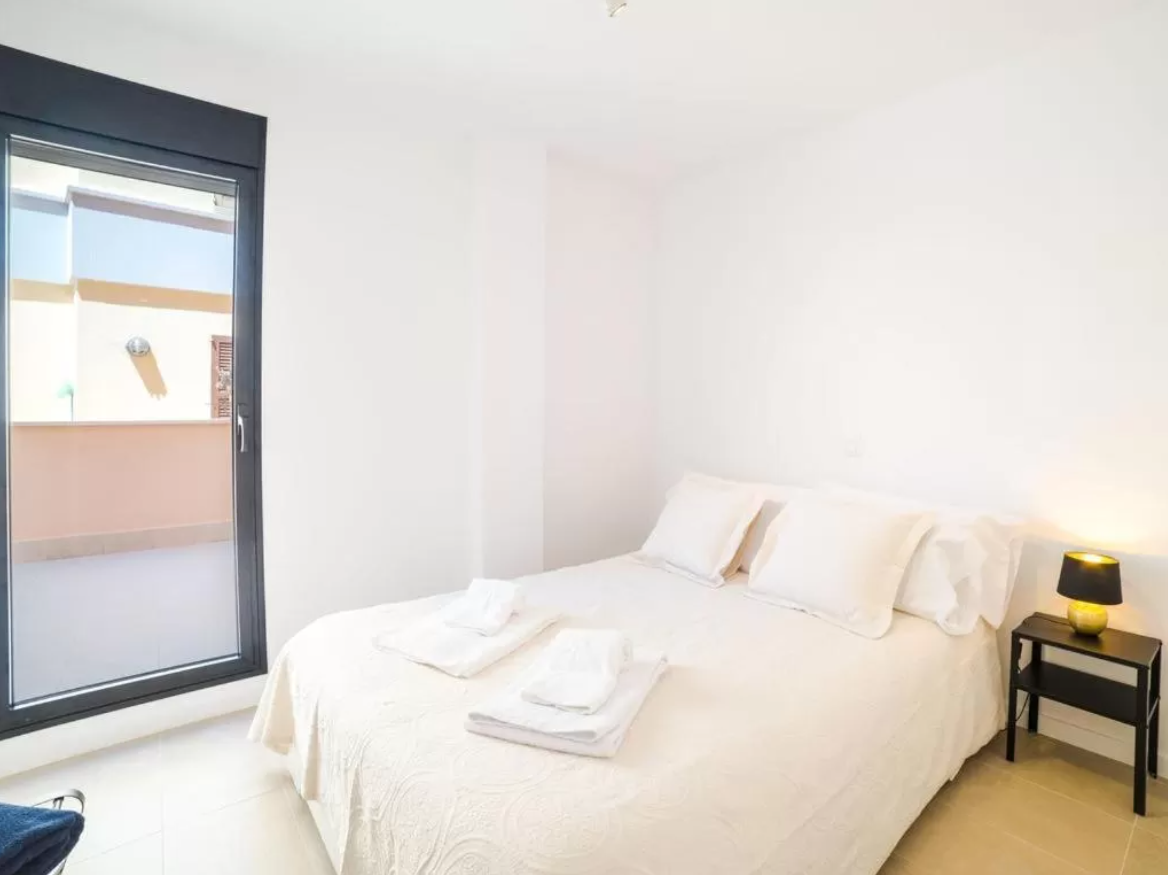 Un dormitorio con cama, mesita de noche, lámpara y ventana.