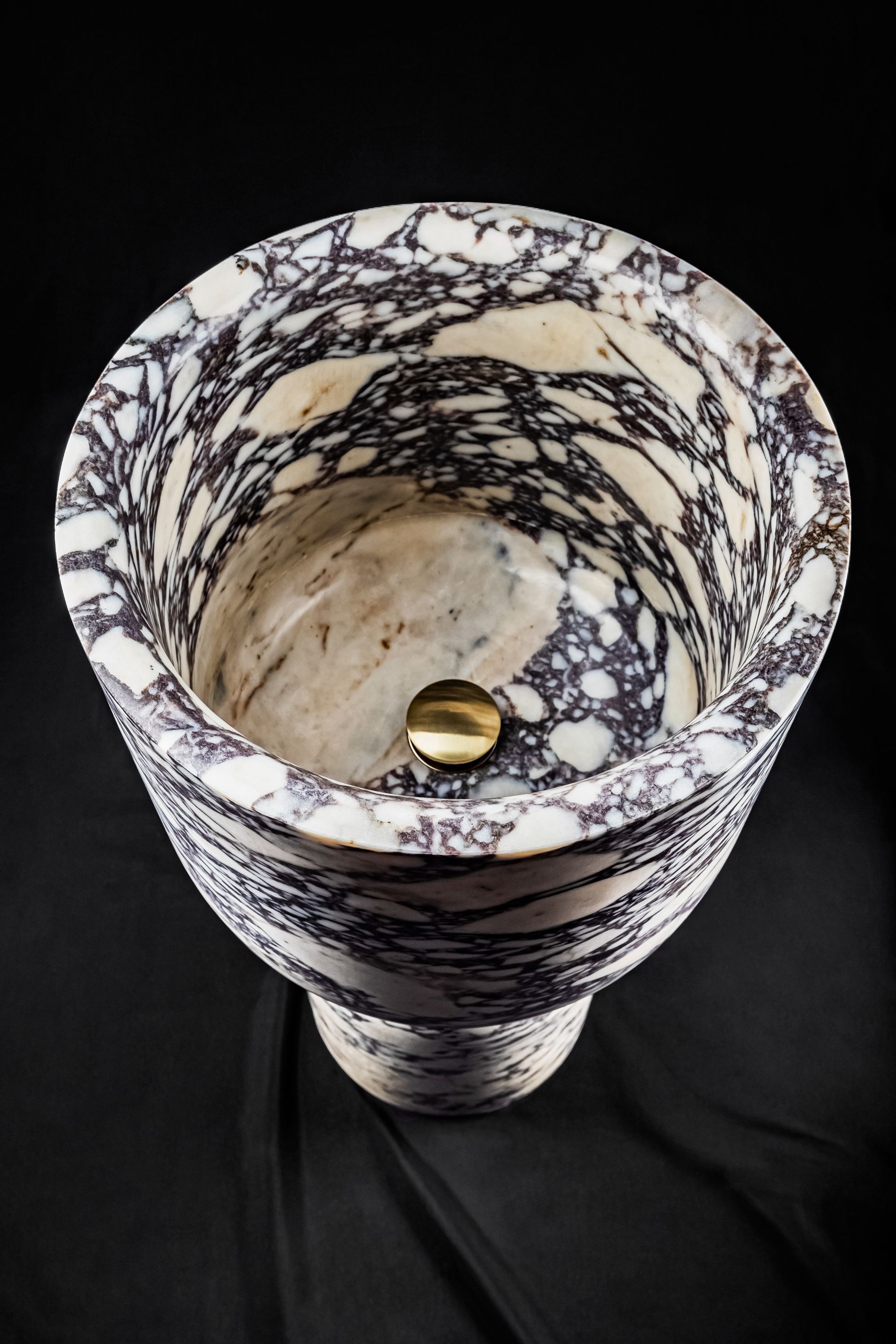 Un lavabo de mármol blanco y negro con desagüe dorado.