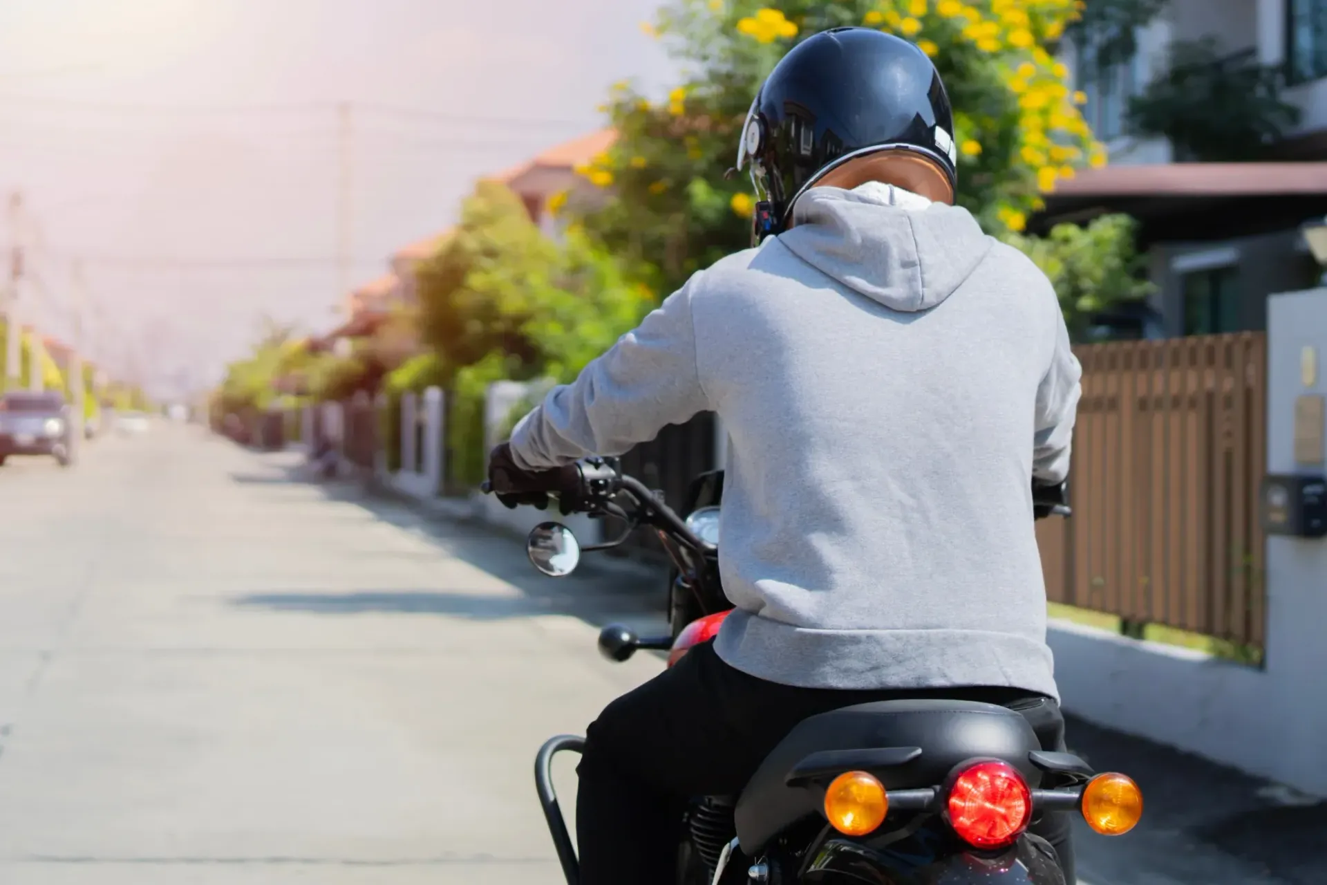 Persona conduciendo una motocicleta por la calle, vistiendo un casco y una sudadera con capucha gris.