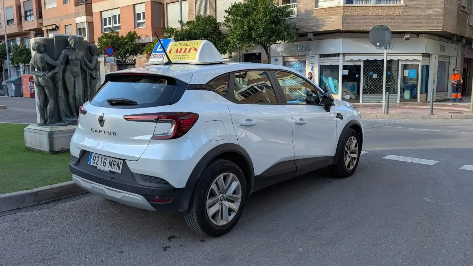 Autoescuela de color blanco estacionado frente al edificio 