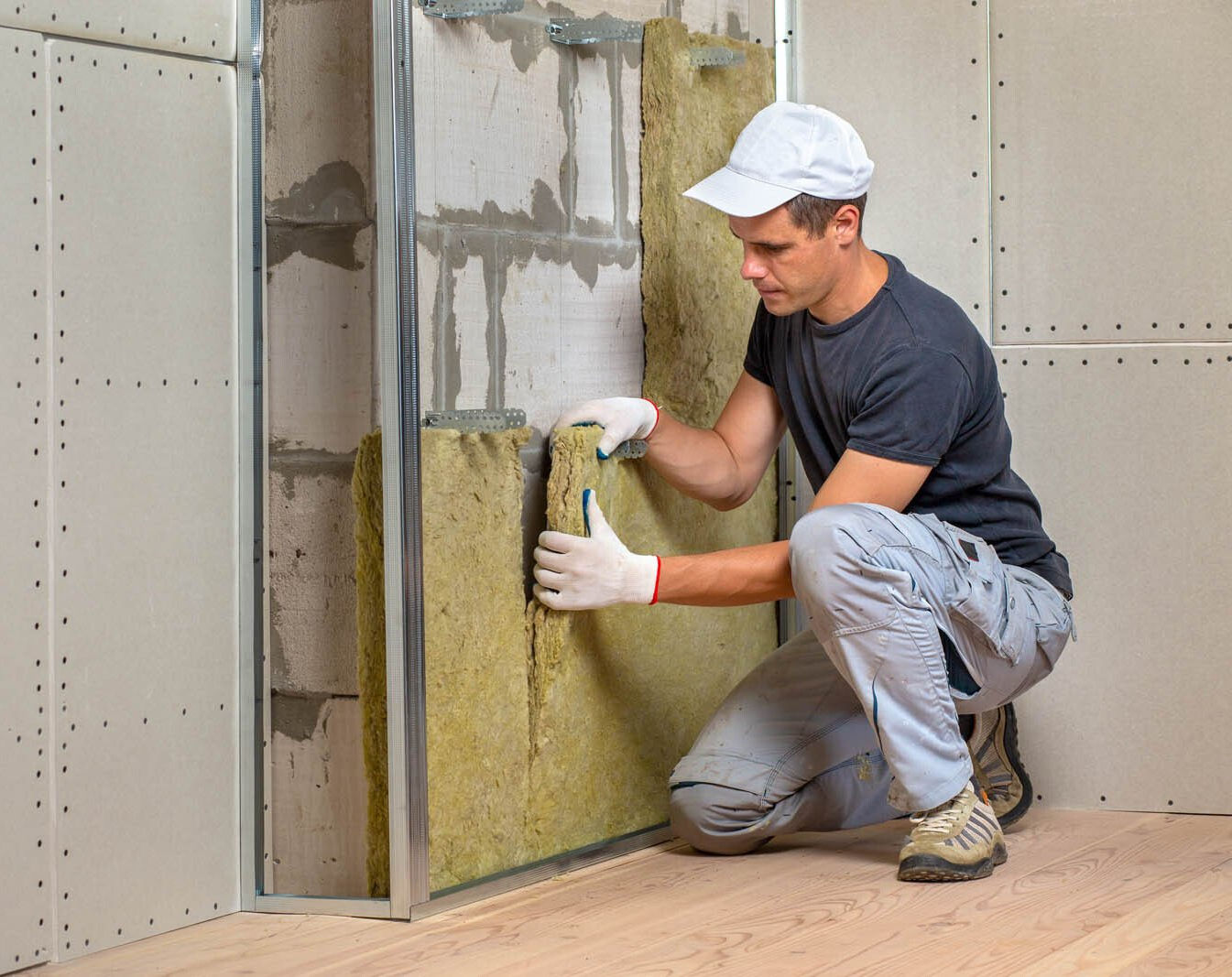 Un homme installe de l'isolant entre les montants d'un mur ; décor intérieur.