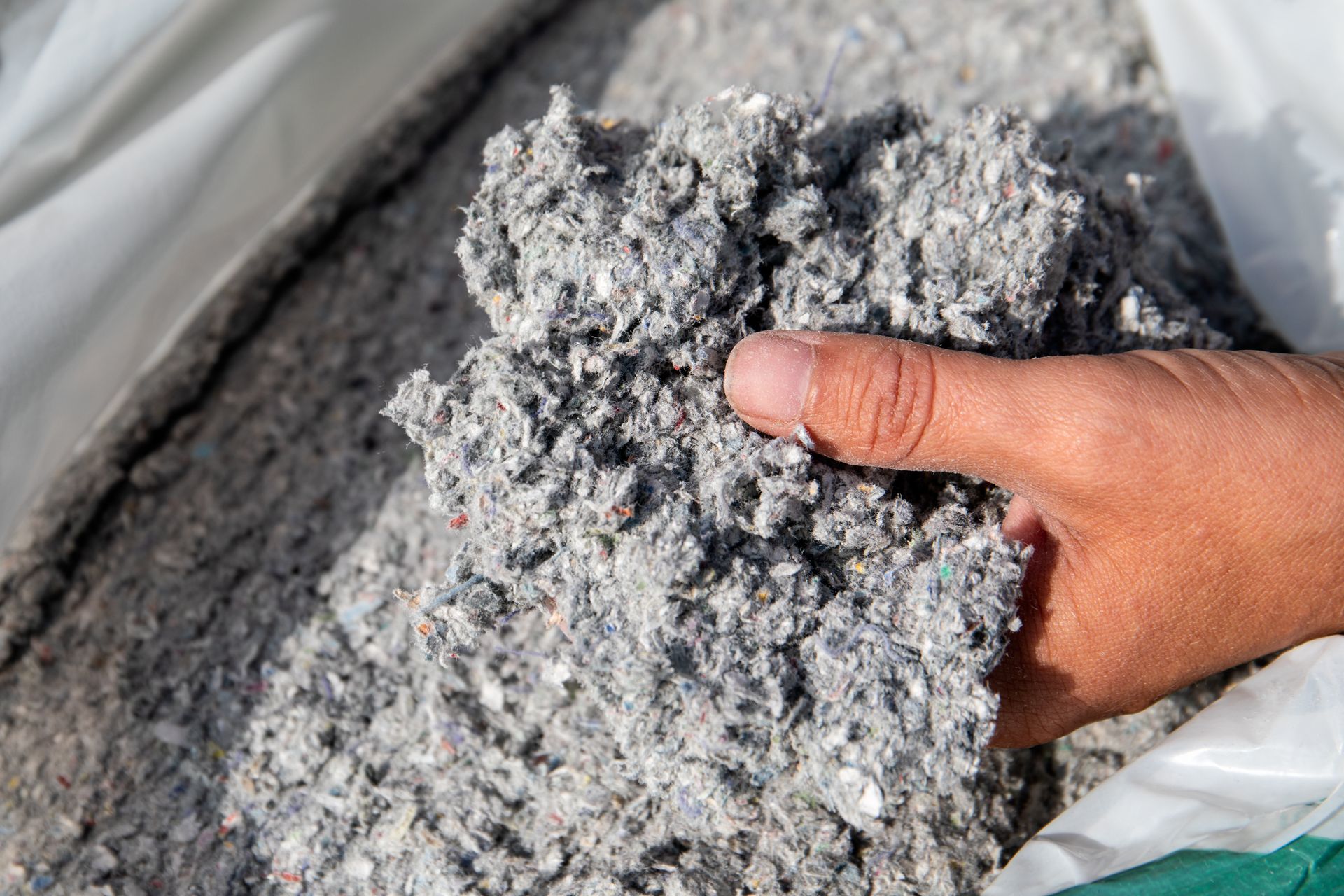 Main tenant un morceau d'isolant en cellulose grise, sorti d'un sac.