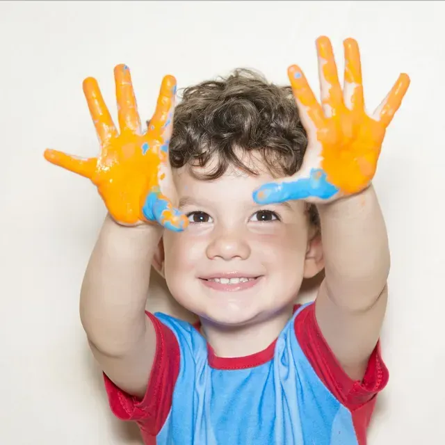 Niño con cabello oscuro tratando de alcanzar burbujas de colores, con la boca abierta por la sorpresa.