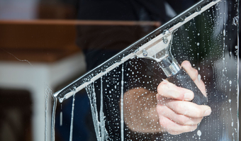 Personne nettoyant une fenêtre savonneuse avec une raclette.