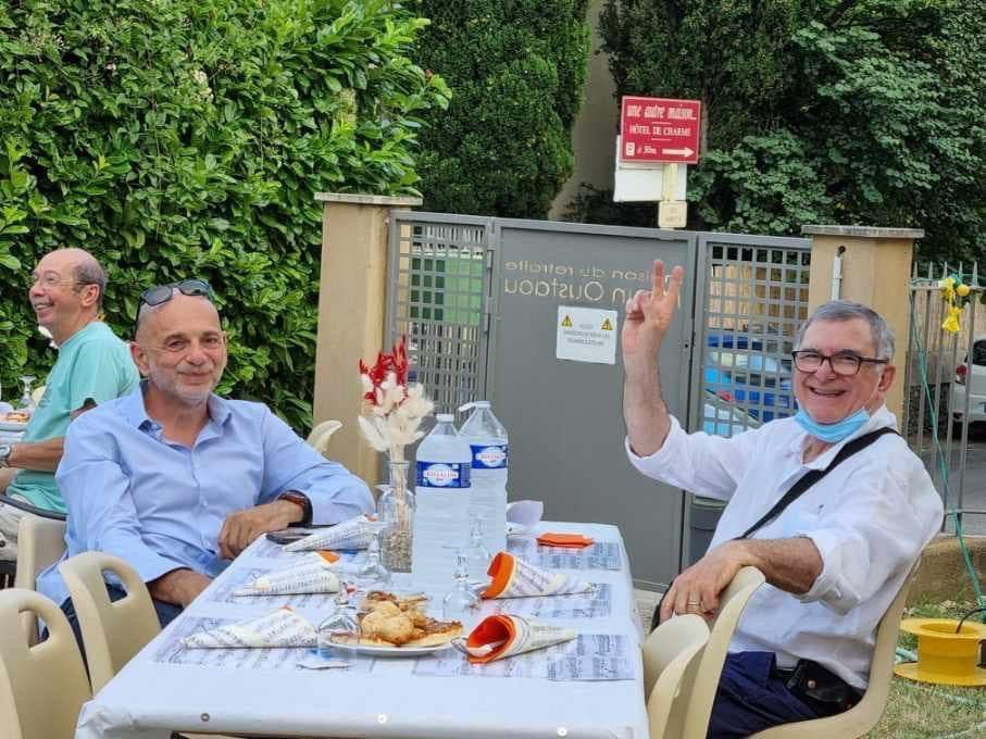 Deux personnes à une table dont l'une fait un signe de la main