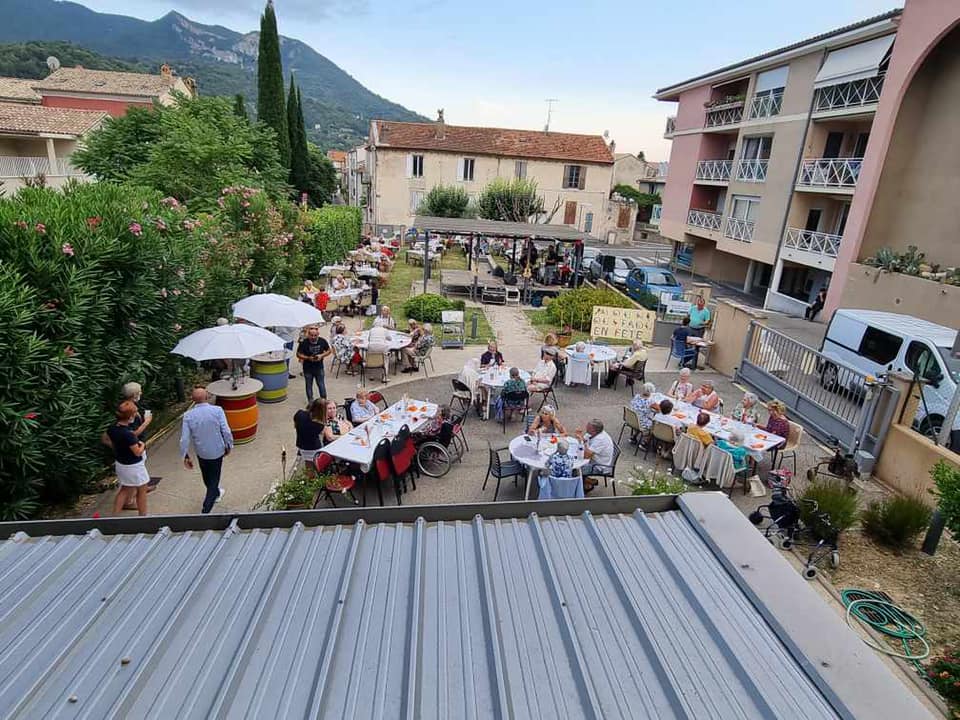 Vue du dessus du parc de la résidence rempli de personnes autour de tables et chaises