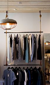 Portant à vêtements dans un magasin de détail avec un luminaire suspendu au-dessus, présentant divers vêtements.