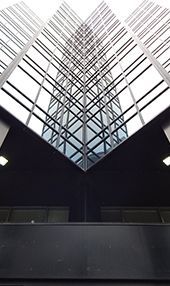 Vue en contre-plongée d'un gratte-ciel en verre avec une façade triangulaire ; cadre en métal foncé, ciel gris.