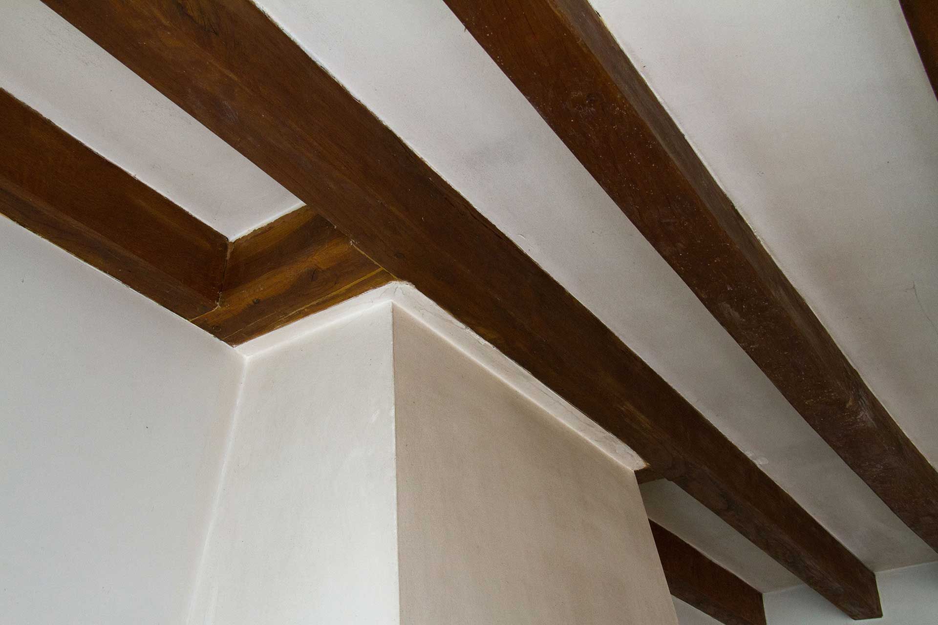 Poutres en bois marron sur un plafond et des murs blancs dans un coin d'une pièce.