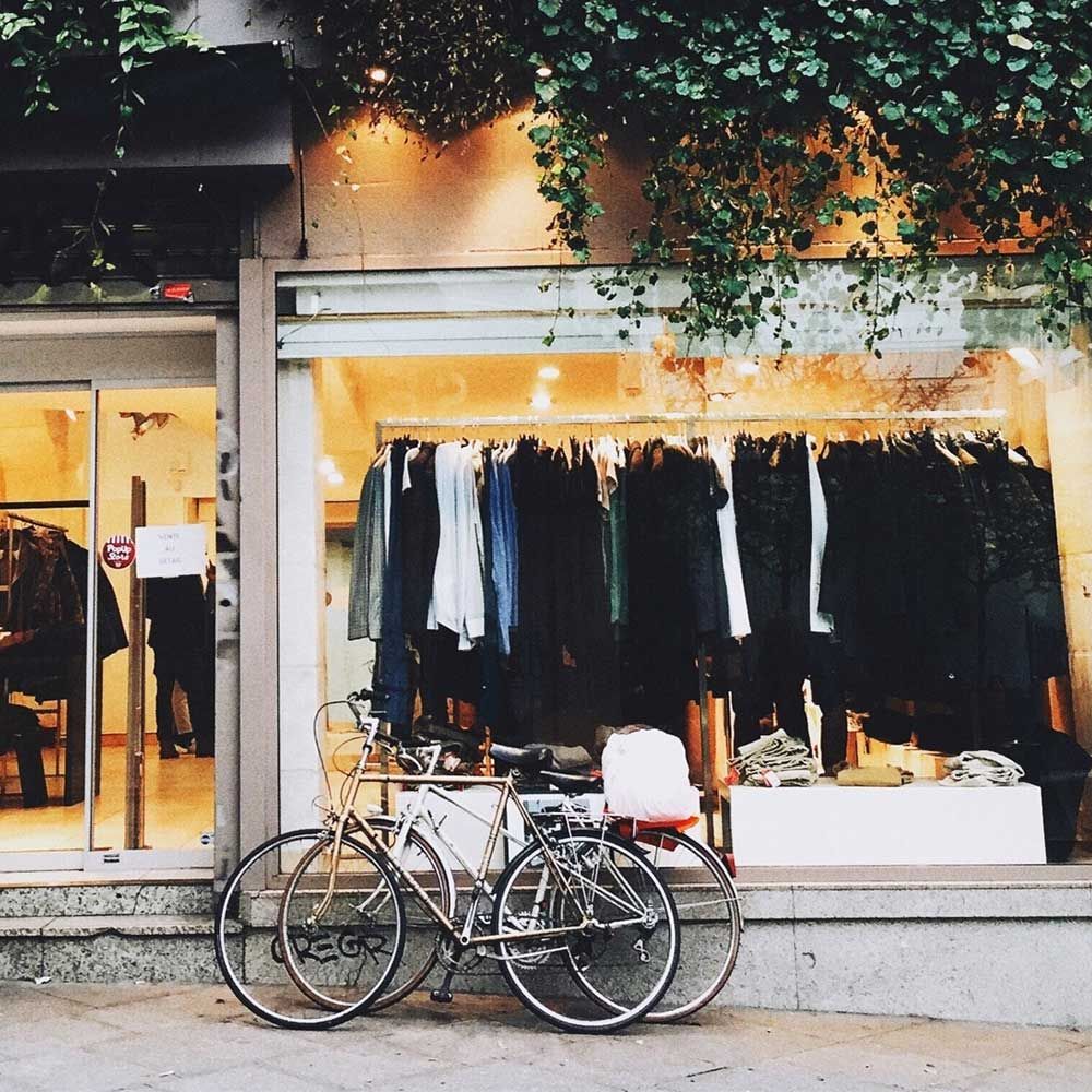 Vélos garés devant un magasin de vêtements avec des vêtements exposés et des plantes suspendues au-dessus.