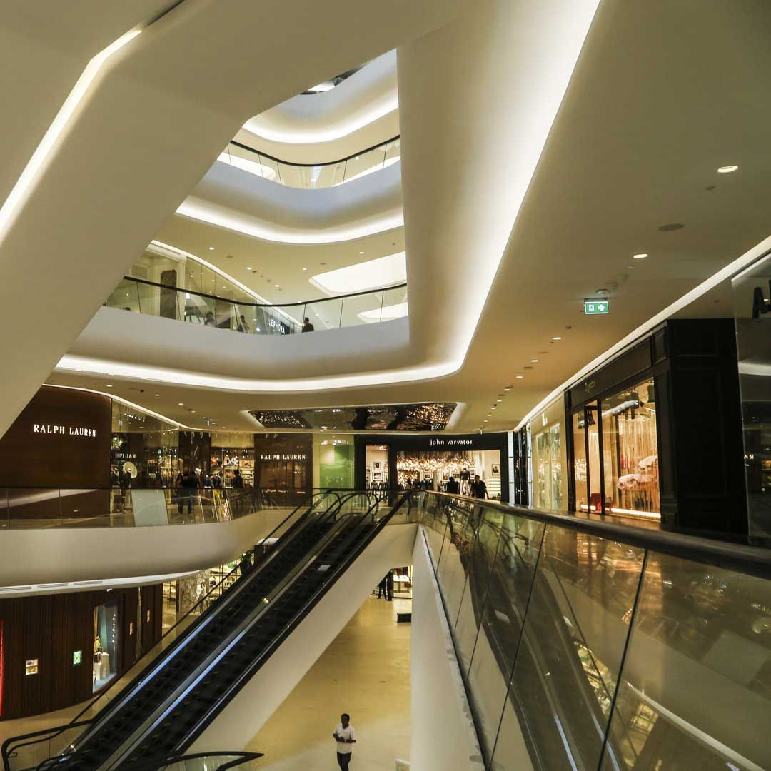 Intérieur de centre commercial à plusieurs étages avec escaliers mécaniques, devantures de magasins et architecture blanche et lumineuse.