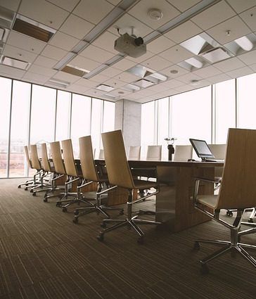 Salle de conférence avec une longue table, des chaises en cuir et de grandes fenêtres. Projecteur au plafond.