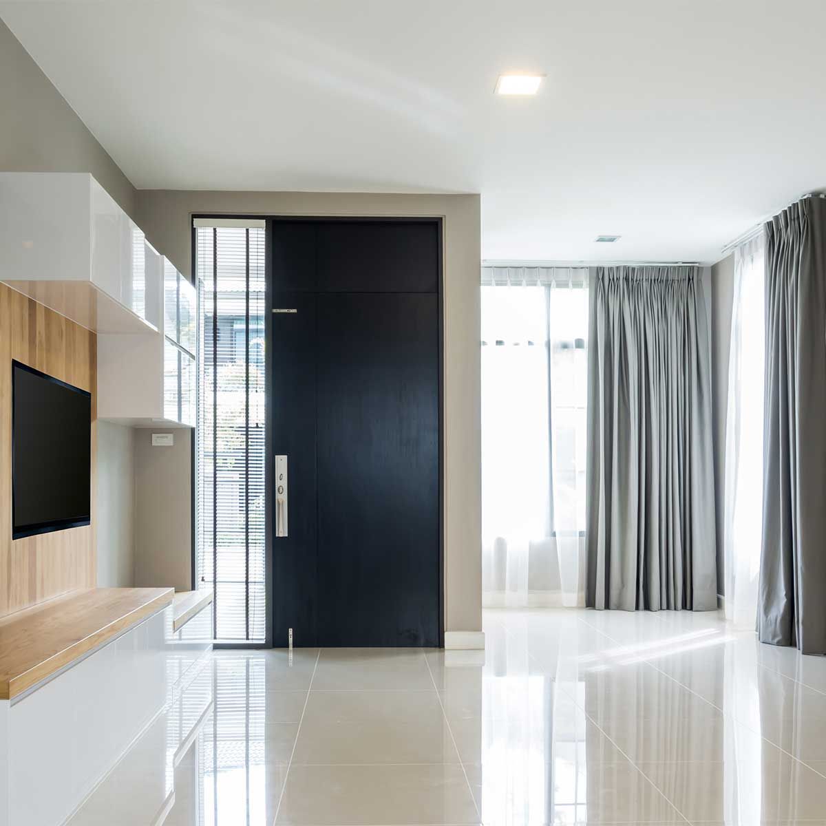 Salon moderne et minimaliste avec porte noire, rideaux gris et sol en carrelage blanc.