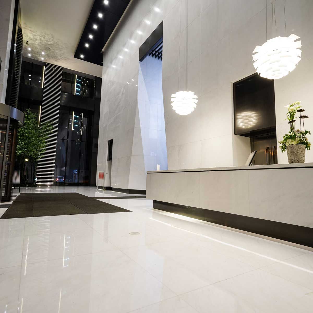 Hall d'entrée moderne avec murs blancs, comptoir de réception et luminaires suspendus décoratifs.