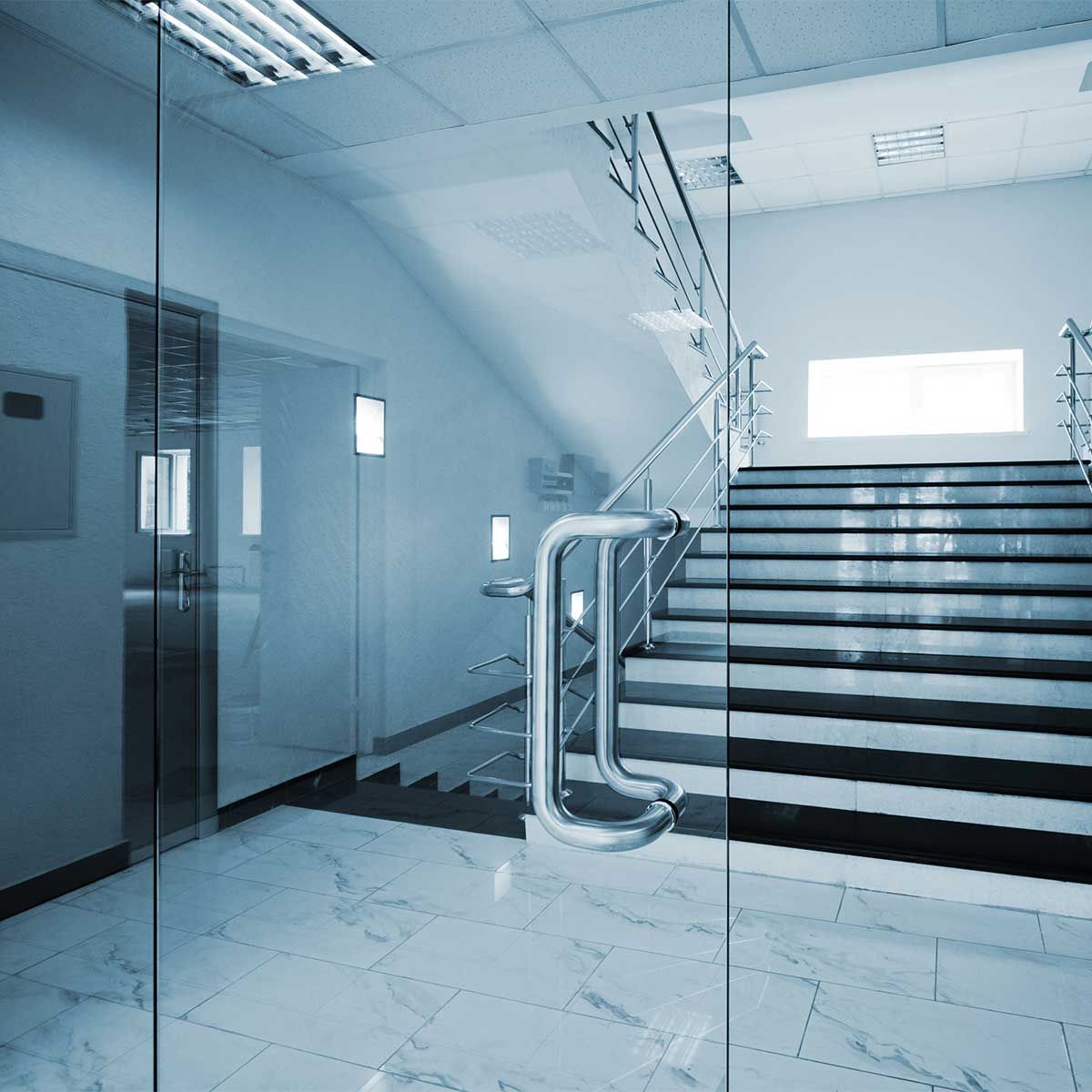 Bureau intérieur aux parois de verre avec escaliers, sols en marbre et éclairage fluorescent.
