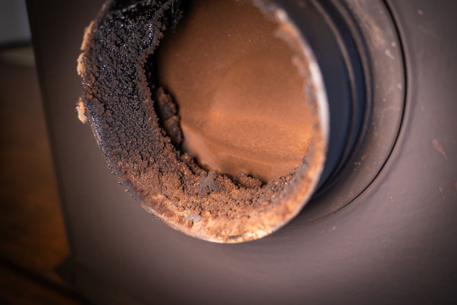 Gros plan sur un conduit de cheminée en métal sombre avec une épaisse couche de suie accumulée à l'intérieur, probablement provenant d'un poêle à bois.