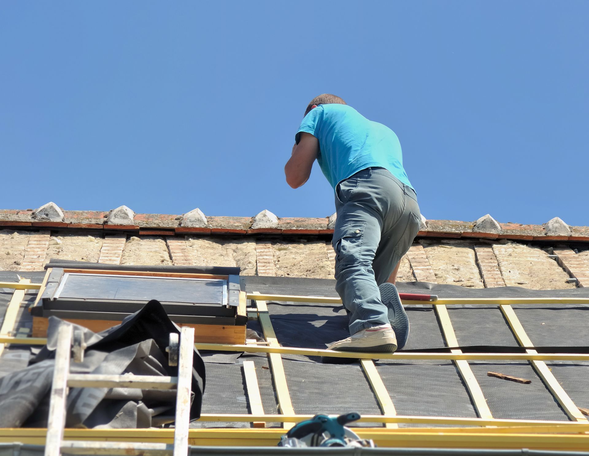 Un homme pose des matériaux de toiture sur un toit sous un ciel bleu.