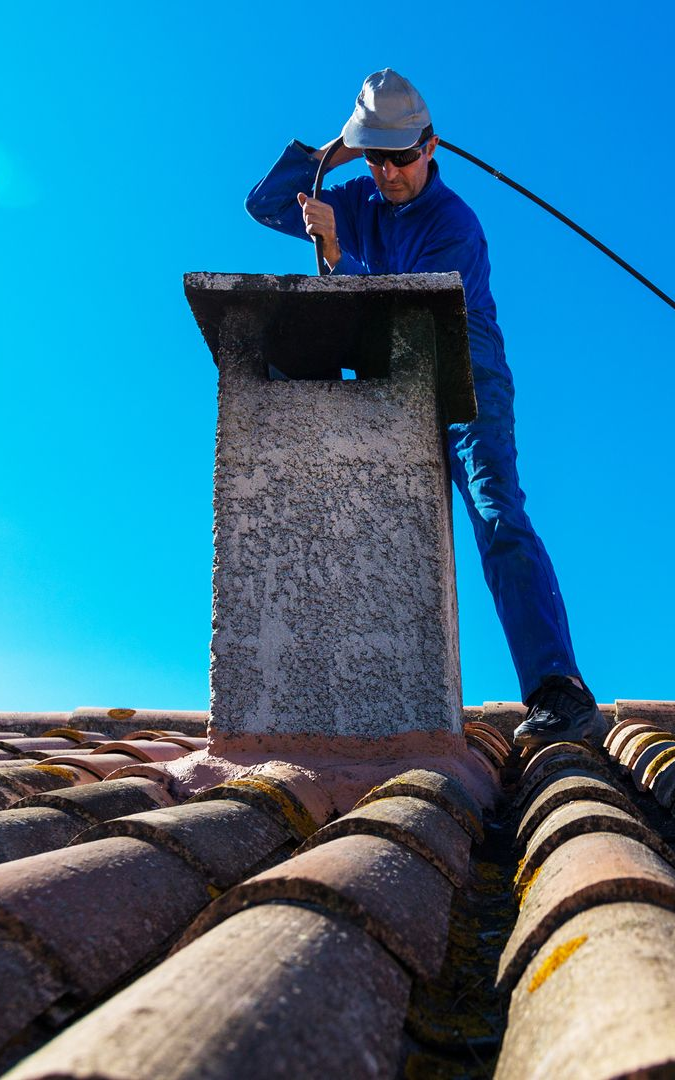 Une personne nettoie une cheminée sur le toit. Ciel d'un bleu éclatant.