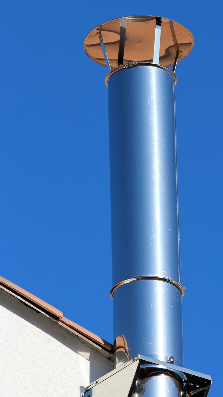 Cheminée métallique brillante se détachant sur un toit et un ciel bleu limpide.