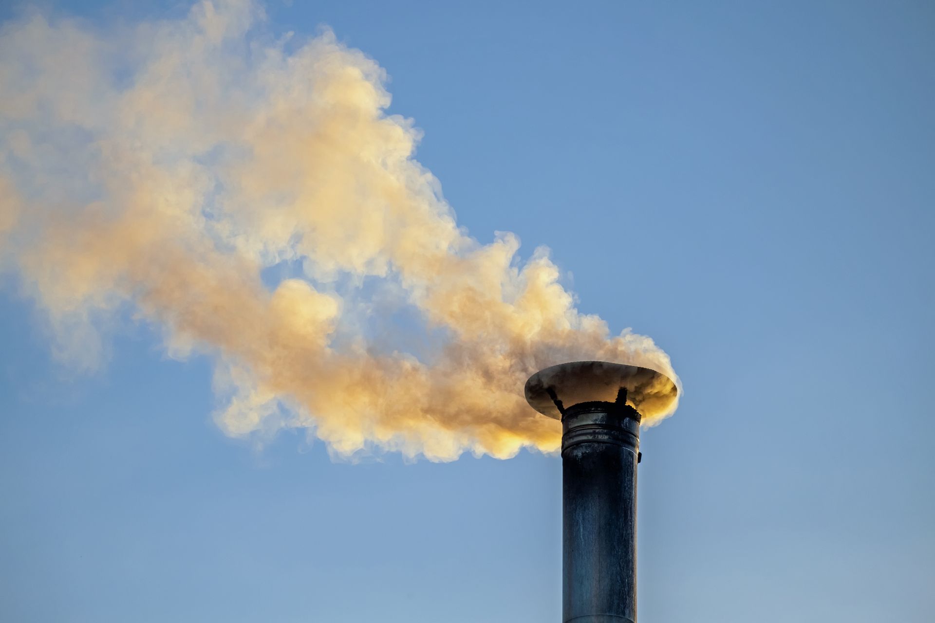 Cheminée crachant une épaisse fumée jaunâtre sur un ciel bleu limpide.