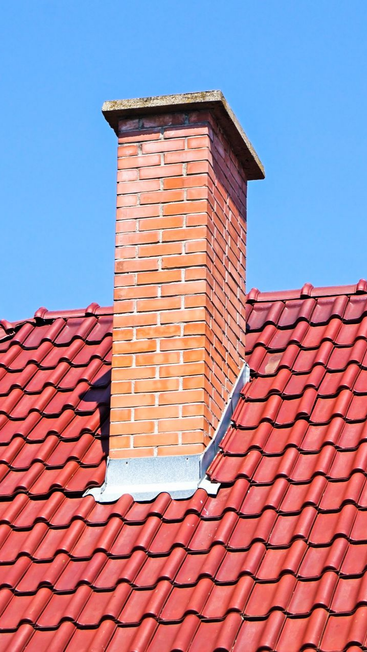 Cheminée en briques sur un toit de tuiles rouges se détachant sur un ciel bleu.