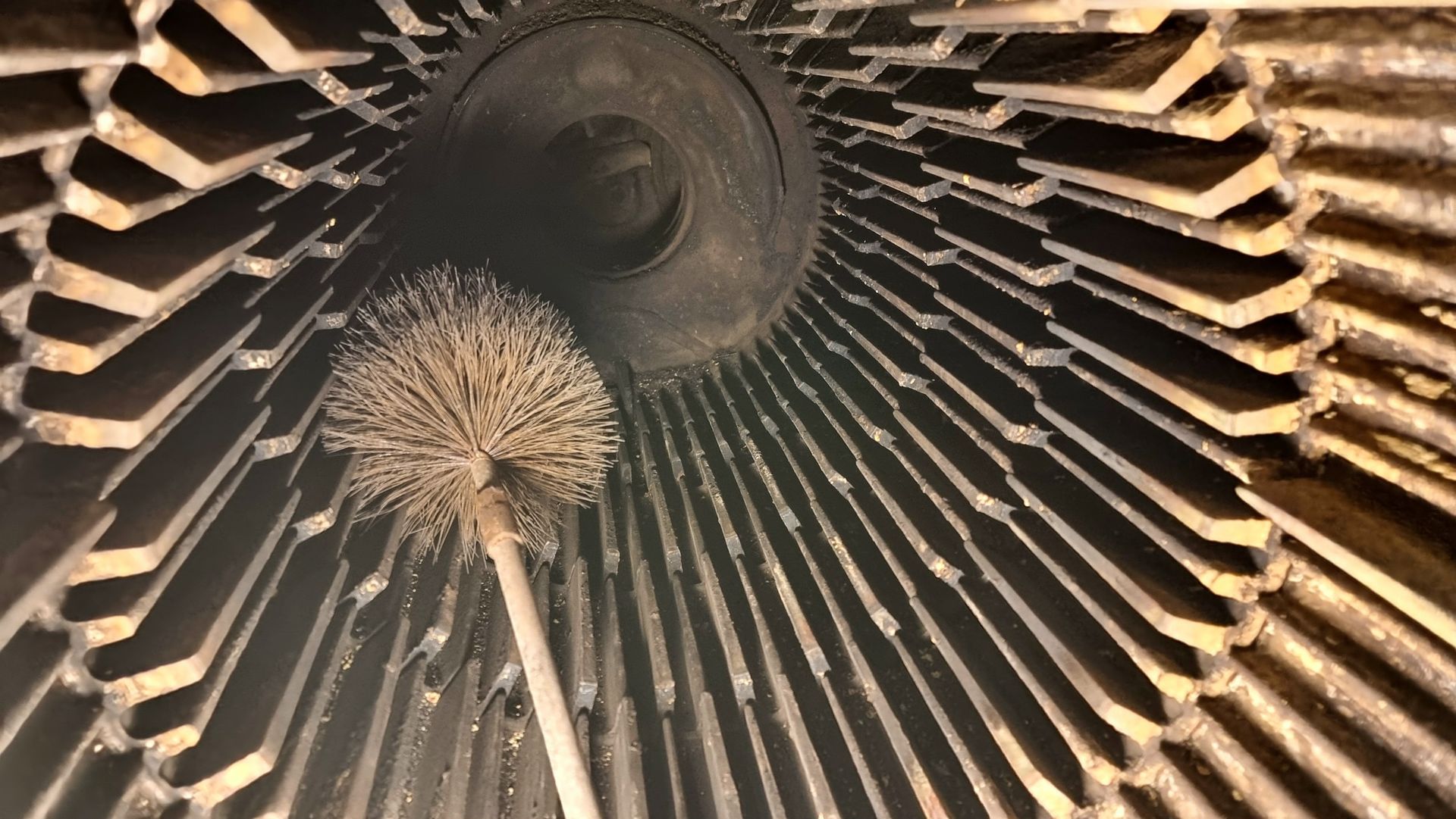 Nettoyage à la brosse de l'intérieur d'une structure cylindrique métallique poussiéreuse munie d'ailettes radiales.