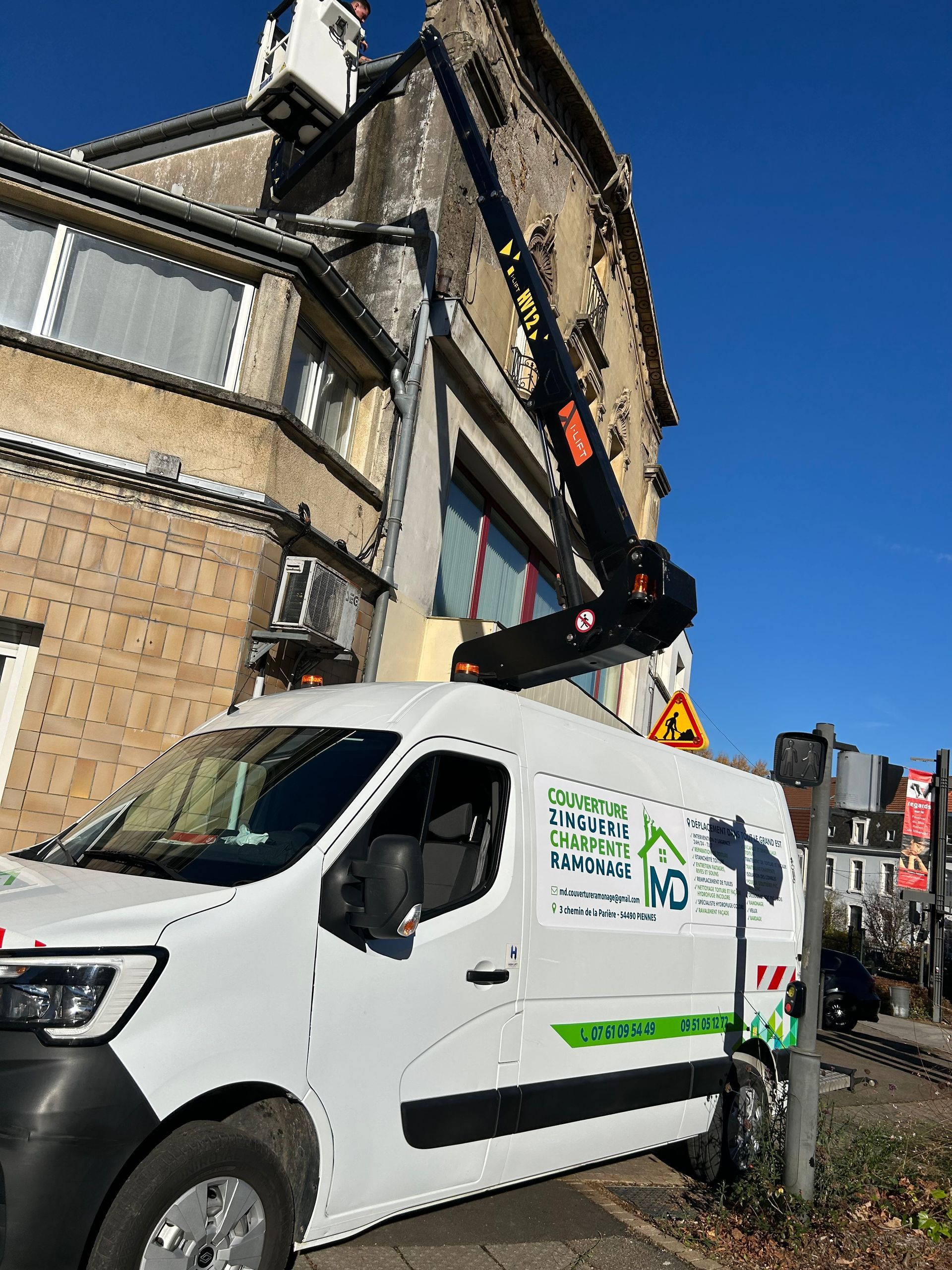 Une personne sur une échelle nettoie une cheminée en briques sur un toit, sous un ciel nuageux.