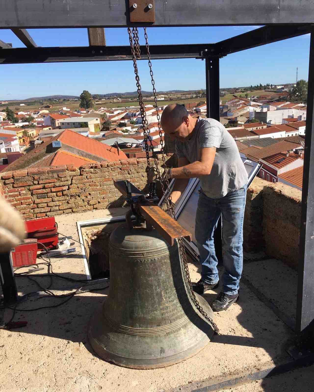 Hombre trabajando en una campana grande, en una azotea con la ciudad visible al fondo.
