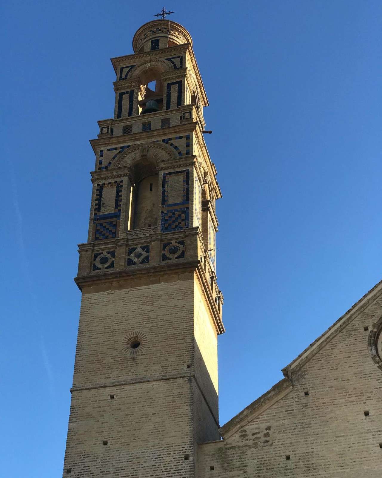 Alto y ornamentado campanario de ladrillo contra un cielo azul brillante.