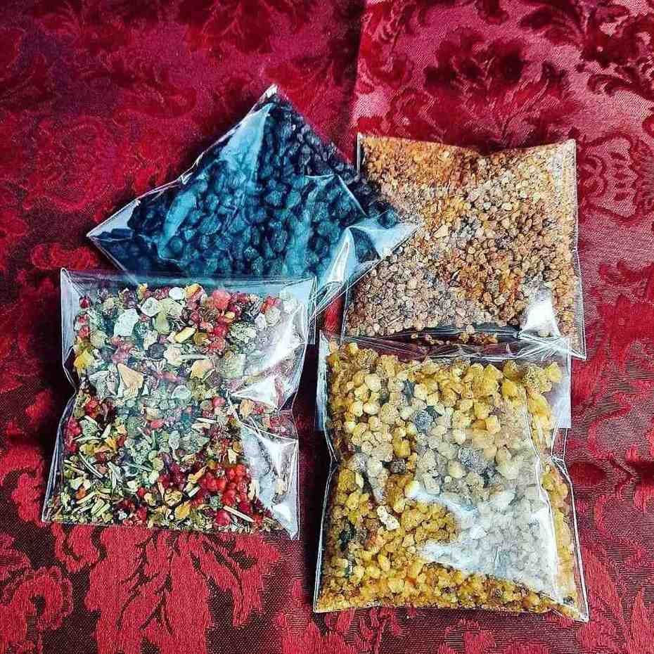 Cuatro bolsas de plástico transparente con hierbas secas y resinas sobre tela estampada de color rojo.