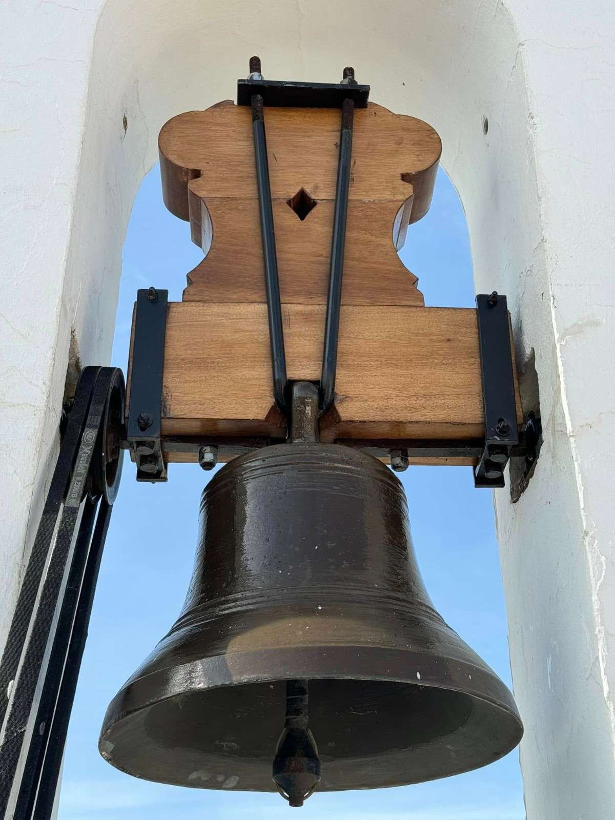 Dos campanas de iglesia desgastadas en una abertura arqueada de un campanario blanco.