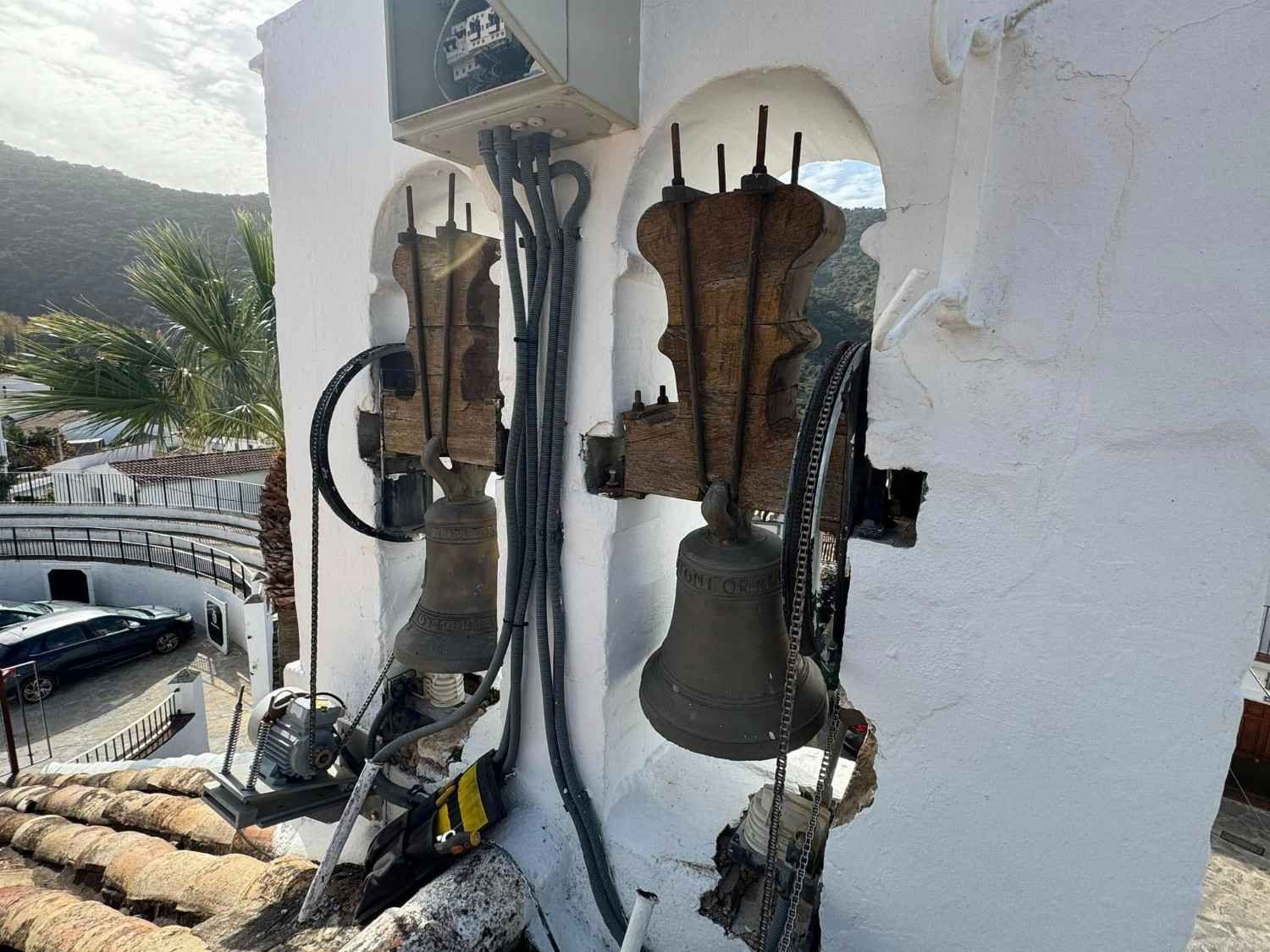 Dos campanas de iglesia desgastadas en una abertura arqueada de un campanario blanco.