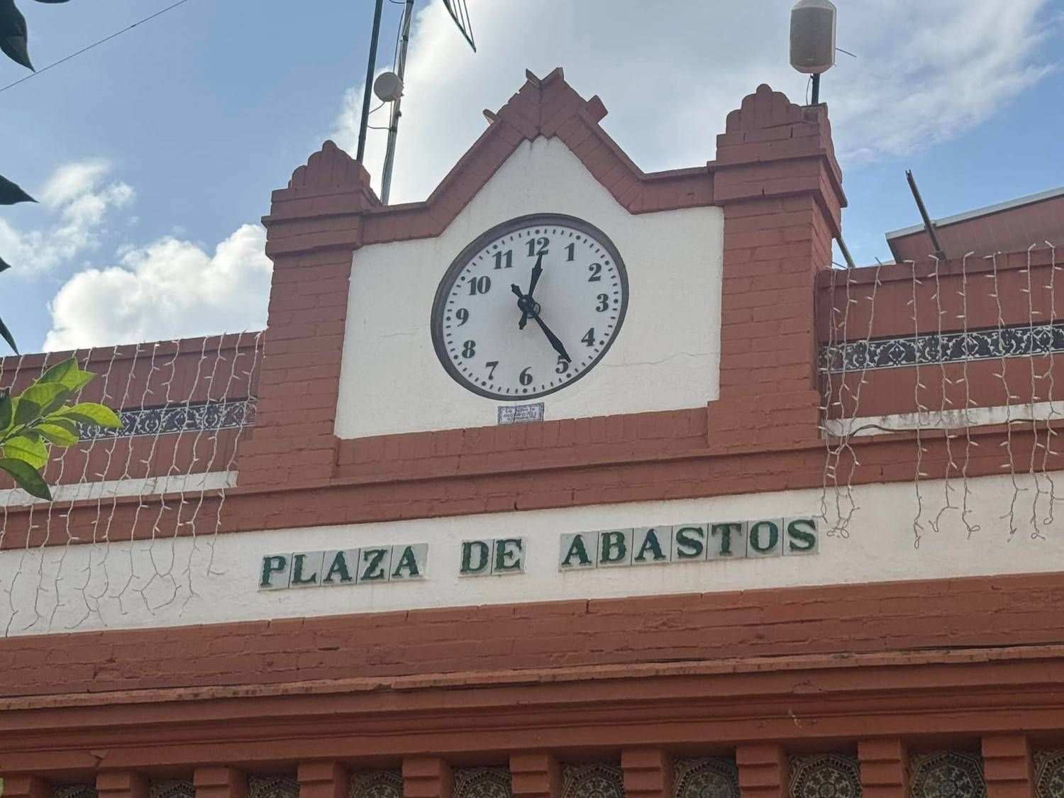 Torre del Reloj de la Plaza de Abastos, con el reloj marcando las 4:56. Edificio rojo y blanco con cielo azul.